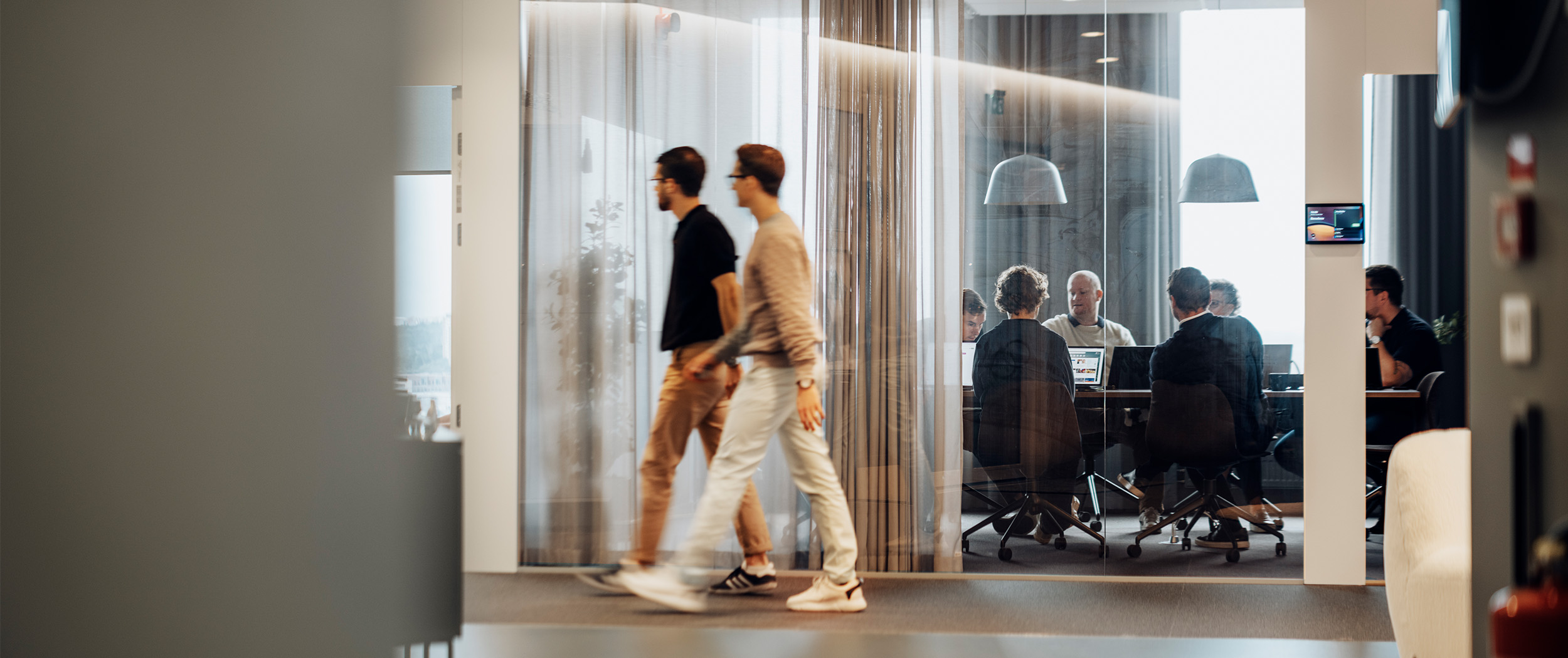 Mötesrum bakom glas med mötesdeltagare och förbipasserande.